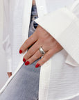 Hand wearing a bold, silver statement ring with an organic pattern, paired with red nails and white shirt over denim, showcasing the Limestone Statement ring's eye-catching design and versatile style.