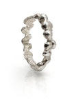 Silver ring with organic, drip-like texture inspired by ocean sand, featuring irregular shapes and contours, reflecting light on its unique surface, standing upright on a white background