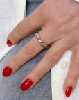 Hand wearing unique silver Sand Drip Band ring with organic, drip-like design, contrasting against red manicure and denim background, showcasing handcrafted jewelry inspired by ocean water-laden sand