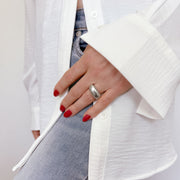 Hand wearing a bold, silver statement ring with an organic pattern, paired with red nails and white shirt over denim, showcasing the Limestone Statement ring's eye-catching design and versatile style.