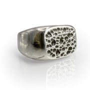 Square silver signet ring with intricate pumice-inspired texture on top, featuring porous pattern reminiscent of cooled lava. Unique statement piece showcasing natural beauty and volcanic inspiration in a stylish, wearable design.