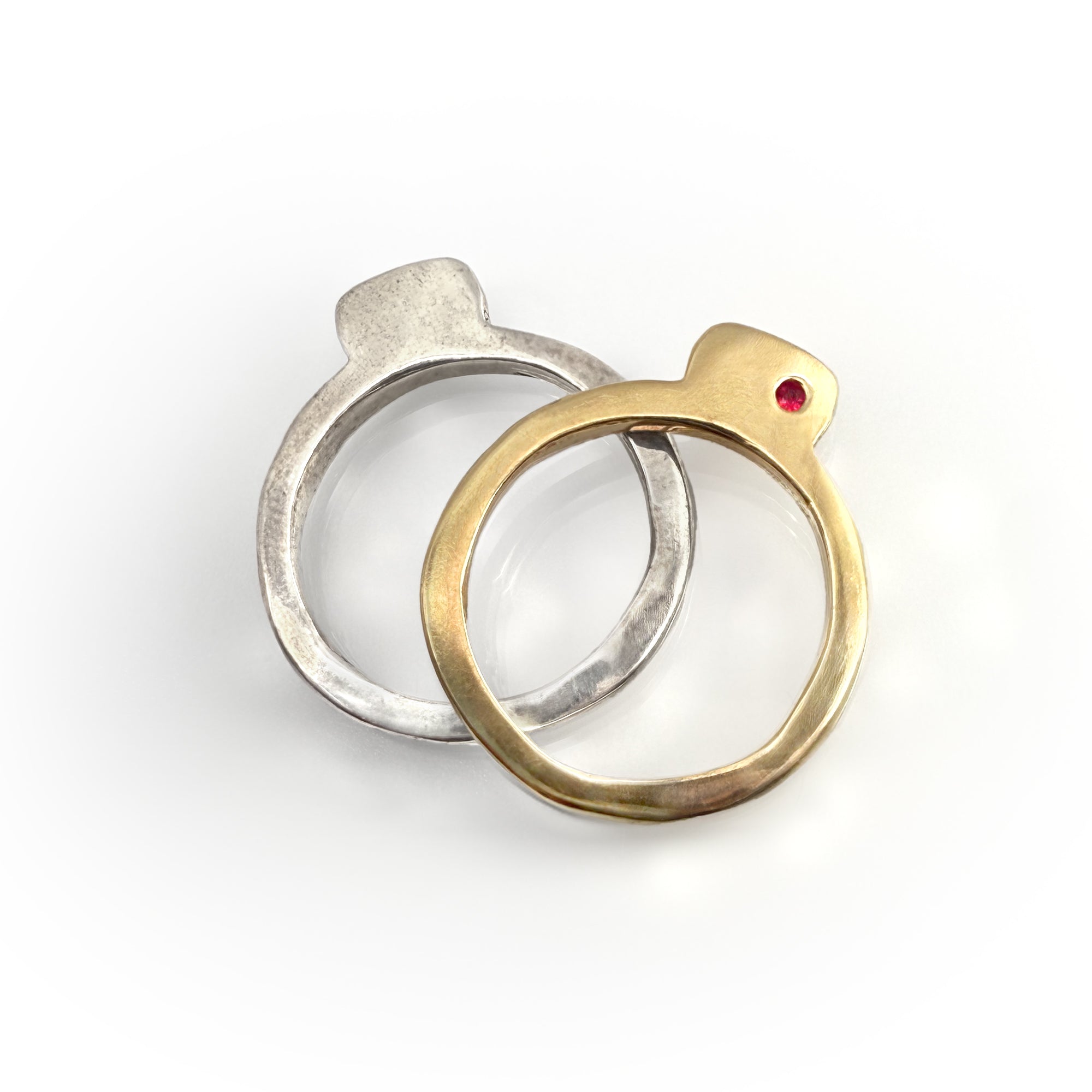 Two Square Splice Band rings, one in silver with a square bevel and one in gold with a red gemstone, showcasing unique handcrafted design for stacking or individual wear