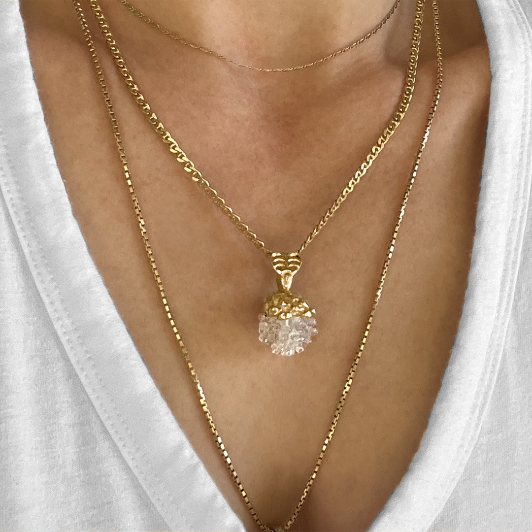 Cherry Pine pendant necklace featuring gold-plated top and clear resin bottom, resembling a pinecone, worn on layered gold chains against a white background, showcasing its unique nature-inspired design and delicate craftsmanship.