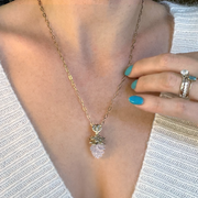 Elegant Mama Pine pendant necklace with gold-plated top and clear resin bottom, worn on a delicate chain over a white sweater, showcased with turquoise nails and a matching ring